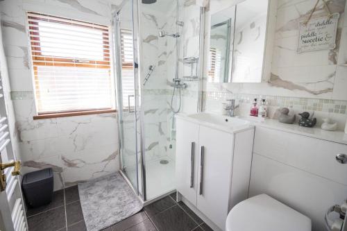 baño blanco con ducha y lavamanos en Stunning Lodge With Free Wifi For Hire At Carlton Meres In Suffolk Ref 60013m en Saxmundham
