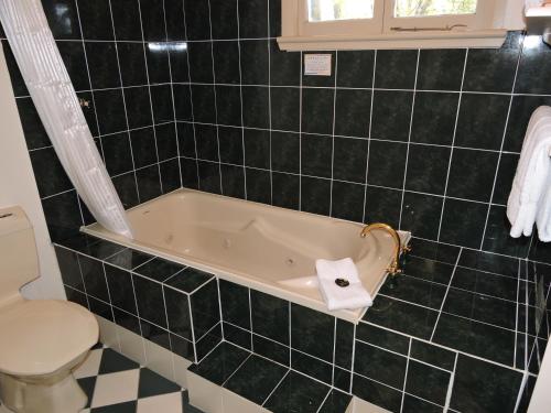 a black tiled bathroom with a tub and a toilet at KUBBA ROONGA GUESTHOUSE - Boutique Luxury Spa Retreat & Gardens - Blue Mountains in Blackheath