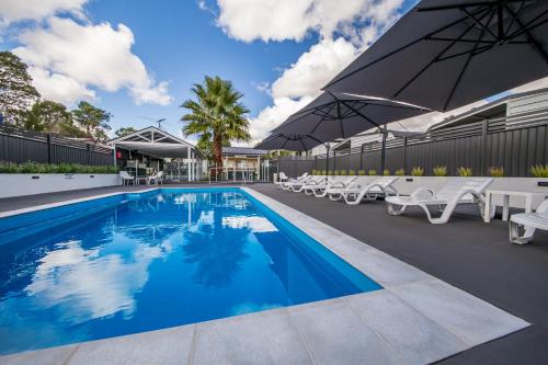 a swimming pool with chairs and umbrellas next to a building at Kingaroy Holiday Park in Kingaroy