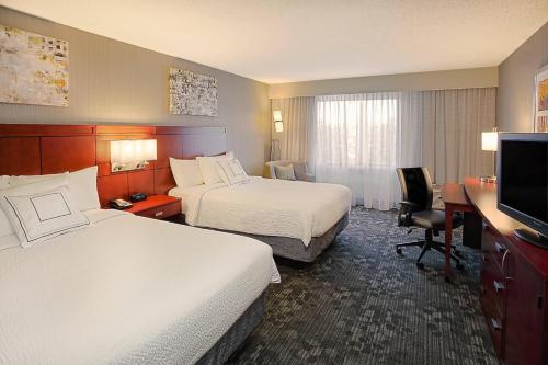 a hotel room with two beds and a desk and a television at Courtyard Mishawaka-University Area in South Bend