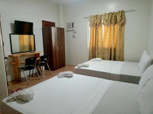 een kamer met 2 bedden, een bureau en een televisie bij RedDoorz @ 4ks Pension House Bogo City Cebu in Banban