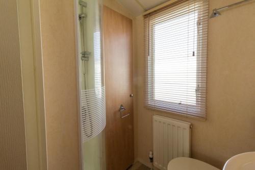 a bathroom with a shower and a toilet and a window at Luxury Caravan For Hire At Hopton Holiday Park With Full Sea Views Ref 80010h in Great Yarmouth
