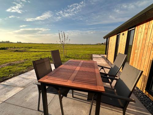 a wooden table and chairs on a porch with a field at Gastenverblijf De Natureluur in Noorden