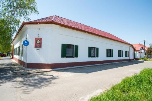 a white building with a red roof on a street at Piros Ponty Panzió in Poroszló