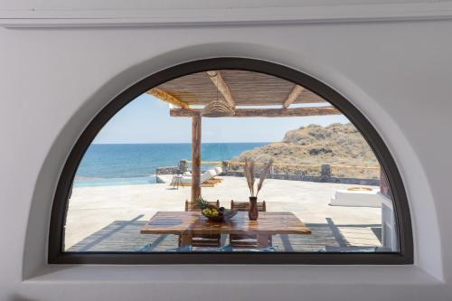an arched window with a table and the view of the ocean at Casa di Mare Luxury Villas in Imerovigli