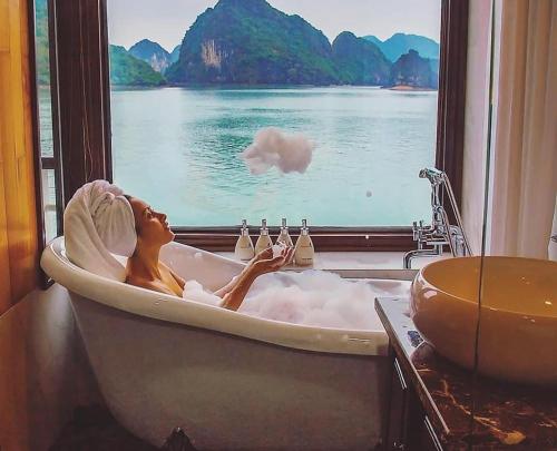 a woman sitting in a bath tub looking out a window at V'Spirit Cruise in Ha Long