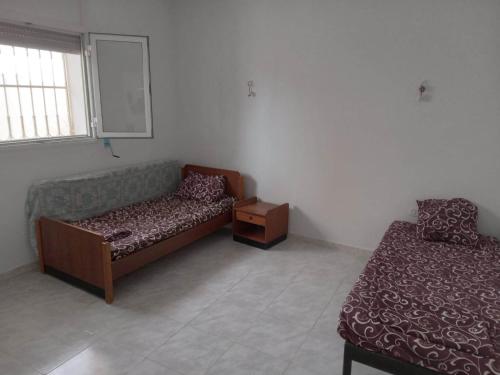 a room with two beds and a table and a window at Confortable Maisonnette prés de la plage à Dar el Alouch in Kelibia