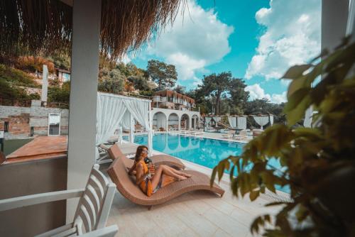 a woman sitting on a chair next to a swimming pool at Zakros Hotel Lykia in Faralya