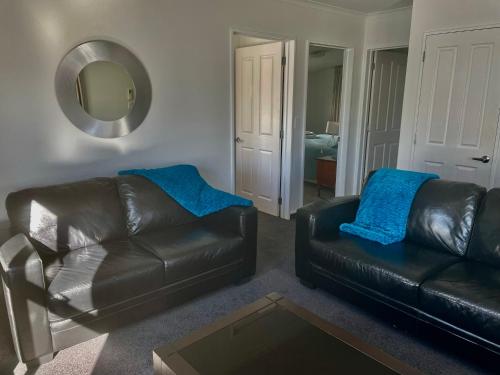 a living room with two leather couches and a mirror at Amberlea Cottages in Hokitika