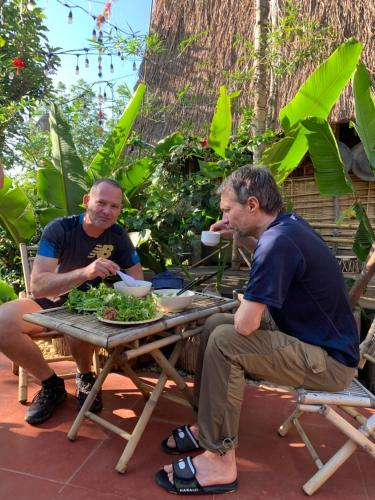 two men sitting at a picnic table eating food at Khu Du Lịch Sinh Thái, Nghỉ dưỡng Homestay Hoàng Ánh - Kon Xom Luh in Kon Tum