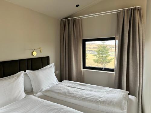 a bedroom with a bed with white sheets and a window at Urriðafoss Waterfall Lodges in Selfoss