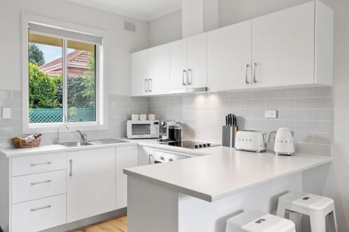 a white kitchen with white cabinets and a window at Kleines Haus Hahndorf in Hahndorf