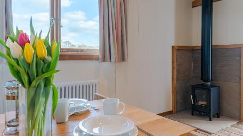 a table with a vase of flowers and a fireplace at Betty Shepherd's Hut in Lydney