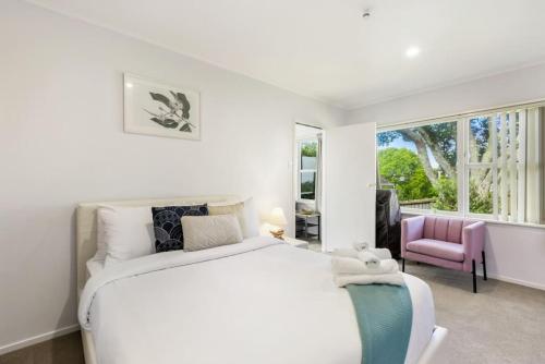 a white bedroom with a large bed and a pink chair at Torbay 1BR Bolthole - WiFi - Seaviews in Auckland