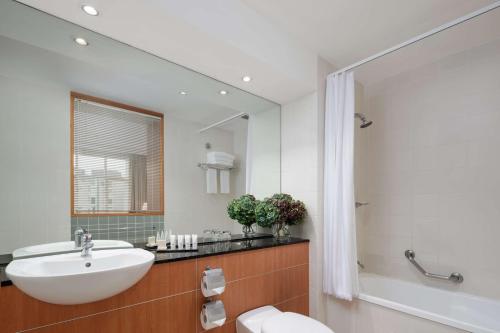 ein Badezimmer mit einem Waschbecken, einer Badewanne und einem Spiegel in der Unterkunft Rydges Newcastle in Newcastle