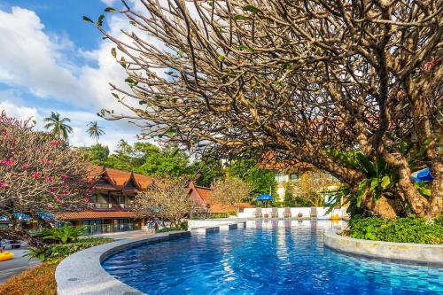 a swimming pool in front of a resort with trees at Diamond Cottage Resort & Spa in Karon Beach