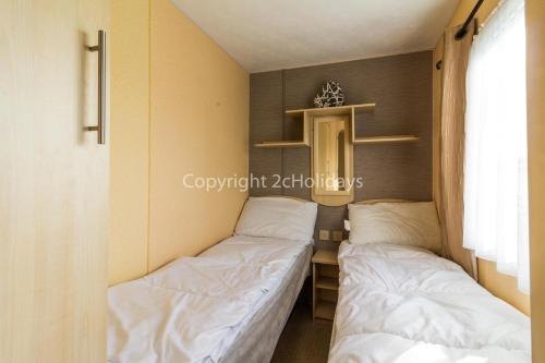 2 camas en una habitación pequeña con ventana en 8 Berth Caravan For Hire By The Beautiful Beach In Heacham, Norfolk Ref 21055a, en Heacham