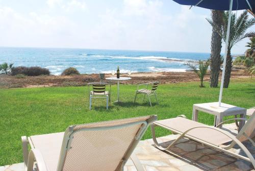 um grupo de cadeiras e uma mesa com um guarda-sol e o oceano em Sea Front Villa With Private Heated Pool, Quiet area Paphos 322 em Kissonerga