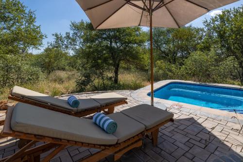 an umbrella and lounge chairs next to a swimming pool at Oase by 7 Star Lodges - Greater Kruger Private 530ha Reserve in Hoedspruit