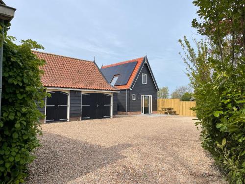 a black barn with a garage and a driveway at Vakantiehuis T Koetshuis in Biggekerke