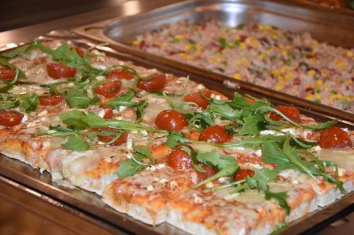 a tray of pizza with tomatoes and greens on it at Hotel SNO Edelweiss in Cerler