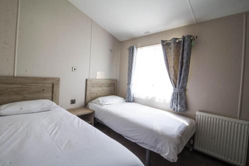 2 camas en una habitación pequeña con ventana en Beautiful 8 Berth Lodge For Hire At Kessingland Beach In Suffolk Ref 90012td en Benacre