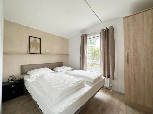 a large white bed in a bedroom with a window at Chalet 527 op Recreatiepark De Wielen in Sint Maarten