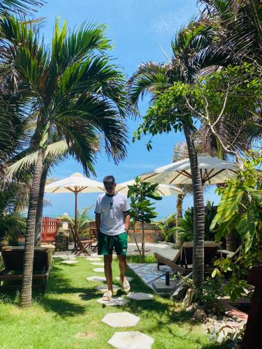 a man walking down a path between two palm trees at Sầm Sơn Boutique Hotel Phan Thiết in Phan Thiet