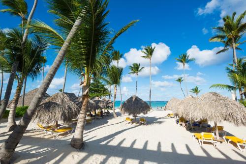 a beach with straw umbrellas and chairs and palm trees at Private Villas with Pool Beach BBQ - BONUS GolfCart FREE April in Punta Cana