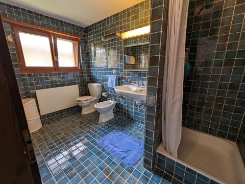 a blue tiled bathroom with a toilet and a sink at Beau Vallon 04 in Crans-Montana