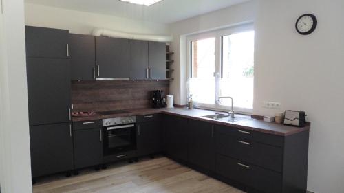 a kitchen with black cabinets and a clock on the wall at Ferienhaus Im Honigdorf in Wietzendorf