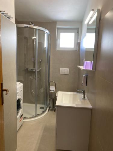 a bathroom with a shower and a sink and a washing machine at Apartmani Tamara - Baška in Baška