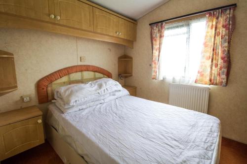1 dormitorio con 1 cama con sábanas blancas y ventana en 6 Berth Caravan For Hire, Minutes From A Stunning Beach In Norfolk! Ref 21036f, en Heacham