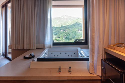 a bath tub in a room with a large window at Mirante da Colyna Hotel & SPA in Monte Verde