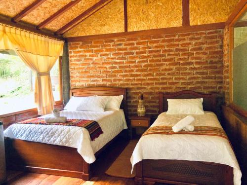 sypialnia z 2 łóżkami i ceglaną ścianą w obiekcie Munay Wasi w Baños