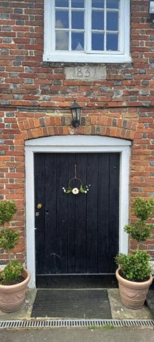 a black door on a brick building with two plants at Plumpton Barn in Ashford