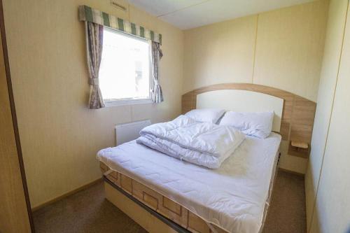 a bedroom with a bed with white sheets and a window at 6 Berth Caravan For Hire With Decking At Manor Park In Norfolk Ref 23017s in Hunstanton