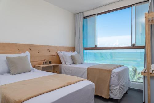 two beds in a room with a large window at Hotel Pousada Aloha in Maceió