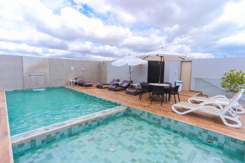a swimming pool with chairs and a table and an umbrella at Pajuçara Praia Hotel in Maceió