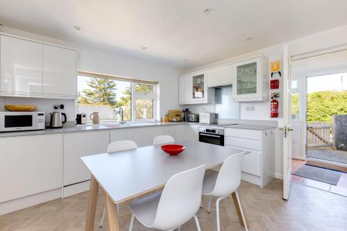 a white kitchen with a table and white chairs at Bella Vista in Polzeath