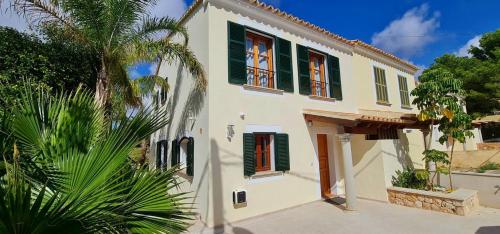 a white house with green shutters and a palm tree at *Casa Aguamarina* Villa am Meer in Cala Pi