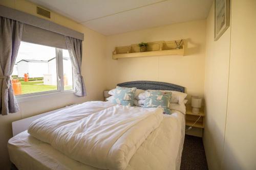 a bedroom with a bed with pillows and a window at Caravan With Decking At Manor Park, Nearby Hunstanton Beach Ref 23013c in Hunstanton