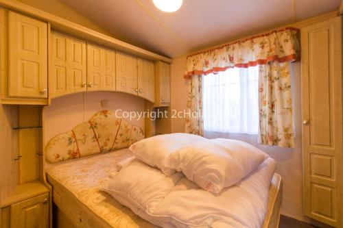 a bedroom with a bed with pillows and a window at 6 Berth Dog Friendly Caravan In Hunstanton, Minutes From The Beach Ref 13013l in Hunstanton