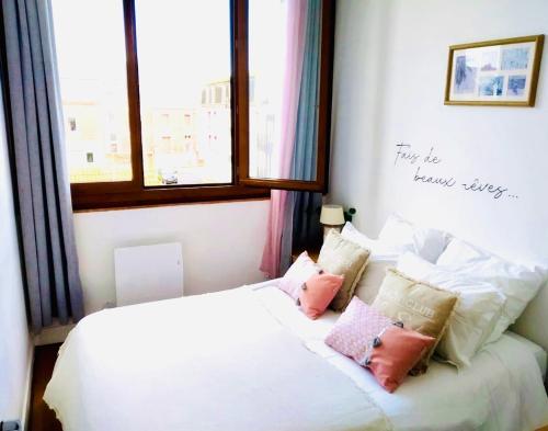 ein Schlafzimmer mit einem weißen Bett mit rosa Kissen in der Unterkunft Le Wood, entre centre ville et plage in Mers-les-Bains