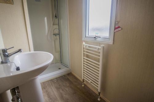 a bathroom with a sink and a window and a shower at Lovely 4 Berth Holiday Home At Felixstowe Beach Holiday Park Ref 55008yc in Walton