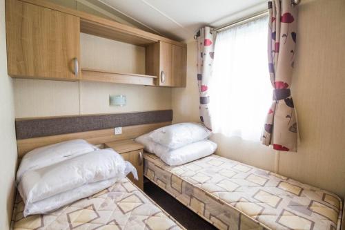 two beds in a small room with a window at Beautiful Caravan For To Hire At Hopton Haven Park In Norfolk Ref 80027t in Great Yarmouth