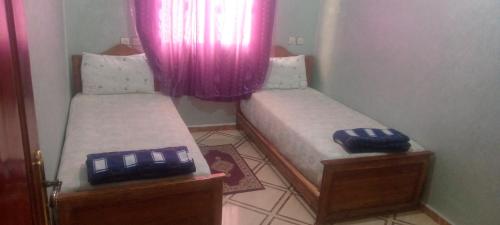 two twin beds in a small room with pink curtains at شقة العتماني للكراء اليومي in Rissani