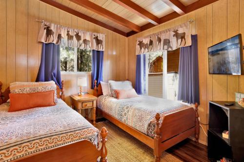 a bedroom with two beds and blue curtains and a tv at Ski View Chalet by Big Bear Vacations Central Moonridge Hillside Retreat in Big Bear Lake