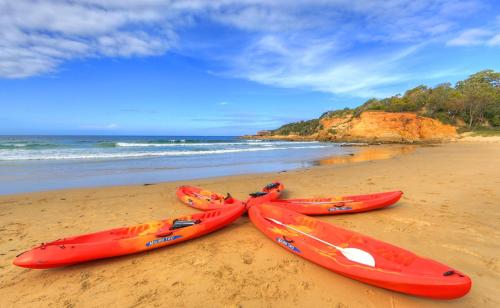 three kayaks sitting on a beach next to the ocean at NRMA Tathra Beachfront Holiday Park in Tathra