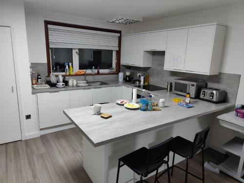 una cocina con armarios blancos y una barra con sillas en Room for rent, en Aberdeen